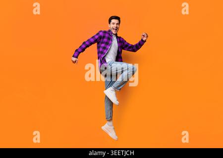 Young Man Jumping Against Bright Orange Background Having Fun Stock Photo