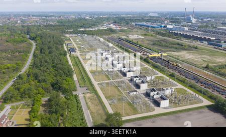 Aerial view of a large electrical substation with high-voltage power lines and concrete structures surrounded by forest and industrial zones in Velsen Stock Photo