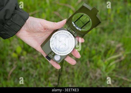 Woman's hand displays the dial of a well-worn compass against a background of green grass. Concept of travel, adventure and navigation. Stock Photo