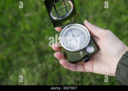 Woman's hand holds an open compass against a background of green grass. Woman navigates her surroundings using the compass. Concept of a travel, adven Stock Photo