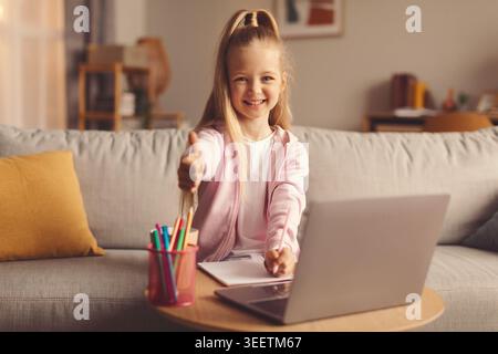 Girl Uses Laptop Sitting on Couch While Holding Colored Pencils in Her Hand Stock Photo