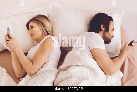 Couple in Bed Using Phones Instead of Talking to Each Other at Night Stock Photo