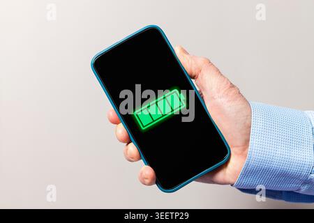 Hand holding a mobile phone with a green fully charged battery indicator on the screen Stock Photo