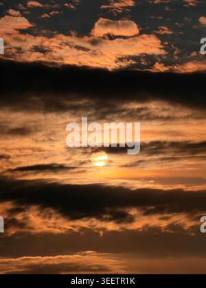 Stunning dramatic sunset sky with dark heavy clouds and golden sun shining through. Moody atmosphere nature background, majestic golden hour view.⁠ Stock Photo
