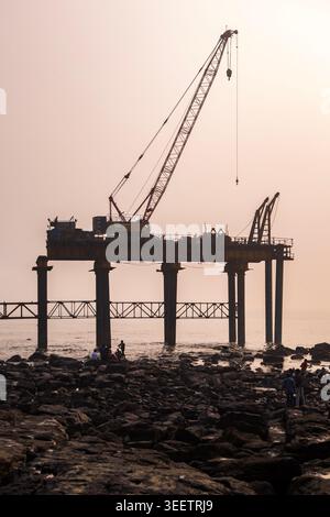 Offshore Crane Structure at Sunset. Coastal Construction Platform with Crane. Marine Construction Site on Rocky Shore. Stock Photo