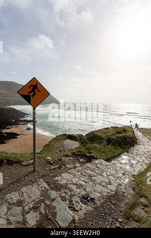 Yellow falling man warning sign above the cliffs at Dunmore Head, Dingle Peninsula, with hikers on the path, County Kerry, Ireland. Stock Photo