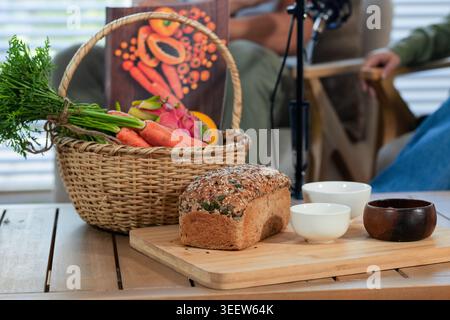 Seeded multigrain loaf resting on wooden cutting board on slatted table, wicker basket nearby Stock Photo