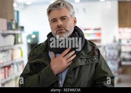 Senior Caucasian man with gray hair and scarf touching his throat while suffering from pain Stock Photo