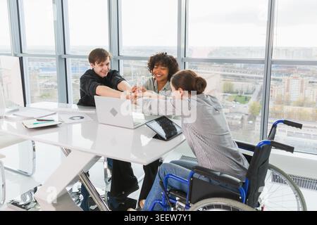 Teamwork brainstorm. Diverse multiracial colleagues woman in chair for people with disability working together. Group of people sitting in creative office discussing business. Young professional team Stock Photo
