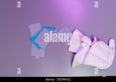 Close-up top view of loose thermal pads with blue backing and white cotton gloves on purple surface, indicating computer maintenance or electronic Stock Photo