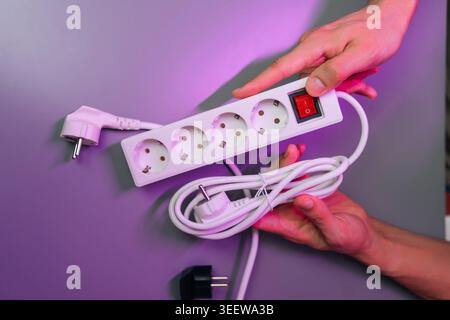 Person holding white power strip with multiple outlets and red on off switch, illustrating energy distribution, household electricity power management Stock Photo