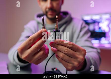 Close-up of male hands holding two different audio jack cables. Musician or sound engineer compares connectors in recording studio with atmospheric Stock Photo