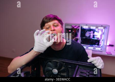 Young technician wearing white gloves pretends to taste CPU chip with tongue out during pc maintenance, upgrade or repair, open computer cases visible Stock Photo