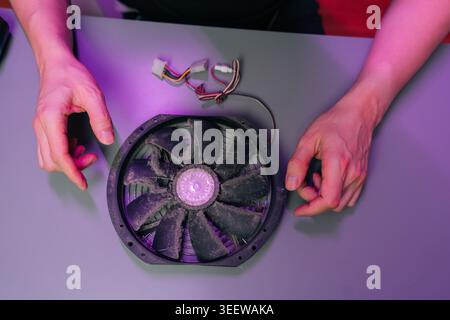 Hands holding dust covered computer cooling fan with wires, being inspected and cleaned during maintenance of obsolete pc hardware and electronics Stock Photo