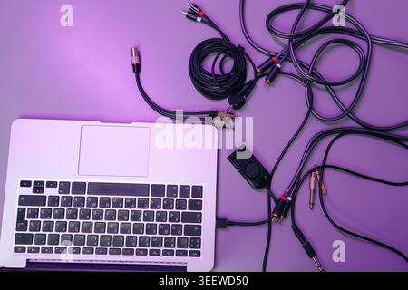 Top down view of music producer DJ workspace. Laptop connected to tangled audio cables, connectors, sound controller on purple surface. Creative Stock Photo