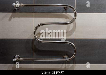 Sleek Chrome Towel Warmer Striped Tiles, Modern Serpentine Radiator Mounted On Glossy Horizontal Tile Bands, Polished Finish Reflects Bathroom Light, Stock Photo