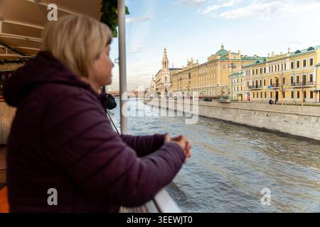 Woman On River Cruise Overlooking Historic Skyline, Hands On Railing, Watching Domed Landmarks And Palace Facades Along Embankment. Overcast Sky Stock Photo