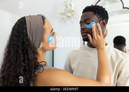 African American couple applying hydrogel patches in bathroom mirror, woman adjusting patch on man Stock Photo