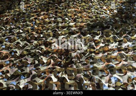 Layered camouflage netting with green and brown patterns creates textured shadows and dappled light, evoking military concealment, outdoor sheltering, Stock Photo