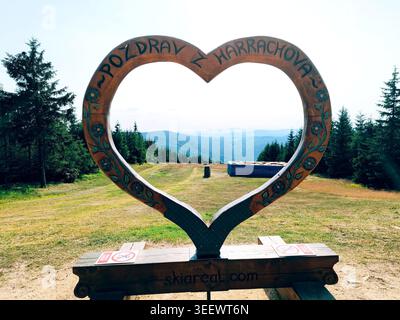Harrachov, Czech Republic, 09.07.2023: Heart-shaped wooden photo frame viewpoint on top of Certova Hora, overlooking forested hills and valley under b Stock Photo