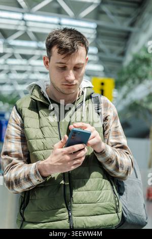 Young male traveler using smartphone while standing in modern airport departure area Stock Photo