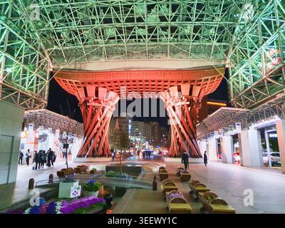 The image captures the iconic Tsuzumi-mon gate at Kanazawa Station in Japan illuminated at night. The massive red wooden structure features a Stock Photo