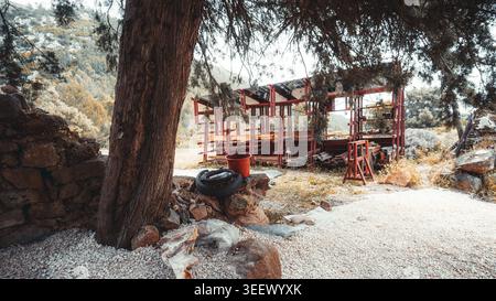 Wide-angle rustic yard with red lumber rack, tree trunk, solar roof elements, pots, and materials for a handmade contemporary rural workspace. Stock Photo