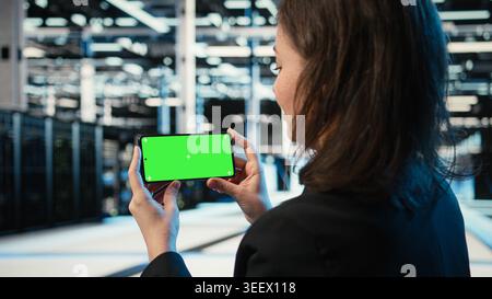 Green screen mockup smartphone used by server hub worker watching videos. Software developer in data center employee holding chroma key mobile phone, looking at online clips Stock Photo