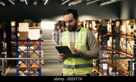 Warehouse employee checking order logistics on tablet in fulfillment center, managing shipment and express delivery details. Man ensuring cargo packages for e-commerce industry, large business. Stock Photo