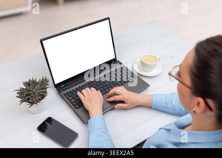 Woman working remotely on laptop with empty display in minimalist workspace, viewed from above with smartphone, coffee and decorative succulent plant Stock Photo