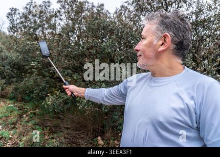 Man enjoying outdoor adventure, using a smartphone on a selfie stick to document his journey in nature Stock Photo