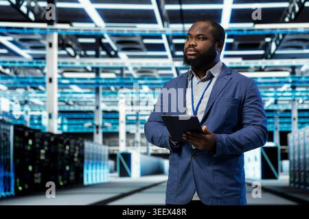 Data center programmer uses tablet to manage database storage rigs. Server farm expert uses touchscreen device to monitor internet cloud computing equipment, technology concept Stock Photo