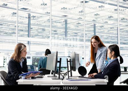 Diverse microchip industrial plant office employees conducting RD study on SoC architecture design. Researchers at PC desk developing innovative semiconductors technology, talking Stock Photo