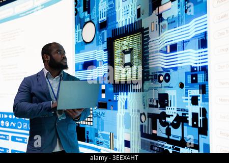 Microchip production plant manager using laptop to upgrade electronic parts displayed on digital wall. African american man looking at semiconductors on screen, researching neural processing Unit Stock Photo