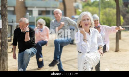 Group of elderly people doing gymnastics together in courtyard Stock Photo