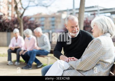 Elderly couple flirting while sitting on bench in courtyard Stock Photo