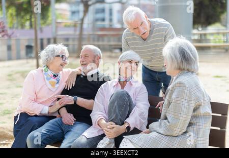 Group of elderly men and women sitting on bench in park and having nice conversation. Stock Photo