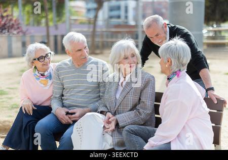 Group of elderly men and women sitting on bench in park and having nice conversation. Stock Photo