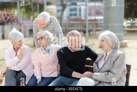 Group of elderly men and women sitting on bench in park and having nice conversation. Stock Photo
