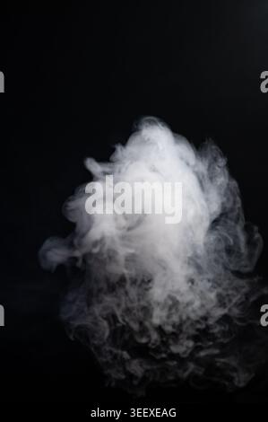 Dense white fog cloud isolated and lifting upward against a black background. Stock Photo