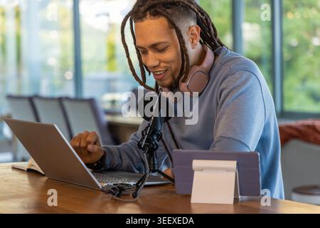 African American man speaking into mic while working on laptop with headphones in cafe Stock Photo
