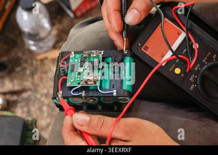 Focused technician hand using digital multimeter tool testing battery pack circuit board repair process measuring voltage current electronics hardware Stock Photo