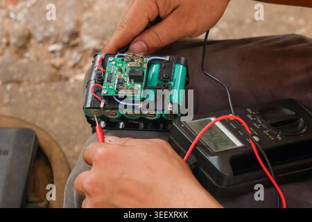Focused technician hands testing custom battery pack using digital multimeter checking electrical circuit board and voltage connection during manual r Stock Photo