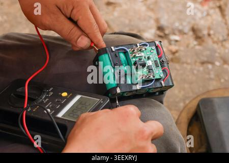 Focused technician testing green battery circuit using black multimeter tool for repair of broken electronics holding wires in careful hands during co Stock Photo