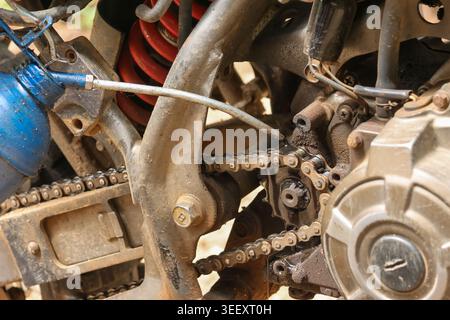 Close up view of person lubricating dirty motorcycle chain with oil from blue bottle showing focused maintenance of mechanical parts on an off road mo Stock Photo