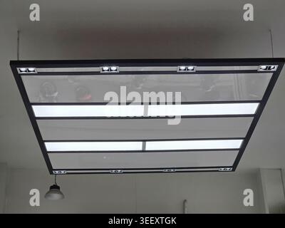 Modern suspended ceiling light fixture radiating bright led illumination across minimalist contemporary room offering calm peaceful atmosphere for int Stock Photo