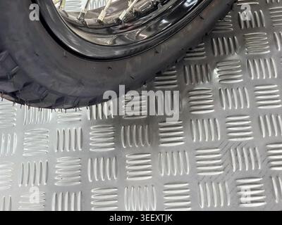 Detailed close up view of black rubber motorcycle tire and wheel resting on sturdy industrial metal diamond plate surface ready for heavy transport co Stock Photo