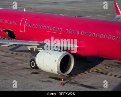 Vibrant red passenger airplane parked on airport tarmac with large jet engine ready for an exciting travel flight. Detailed view showing metal fuselag Stock Photo