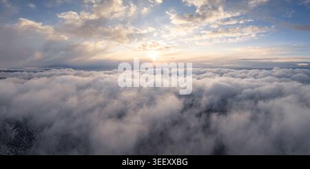 Aerial view of a thick blanket of white clouds under a golden sunset sky with soft light breaking through the horizon. Stock Photo