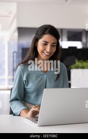 Smiling Brazilian woman using laptop seated at desk Stock Photo